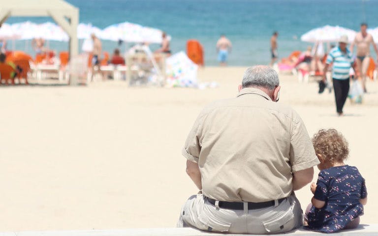 An older man sites at the beach with a child.